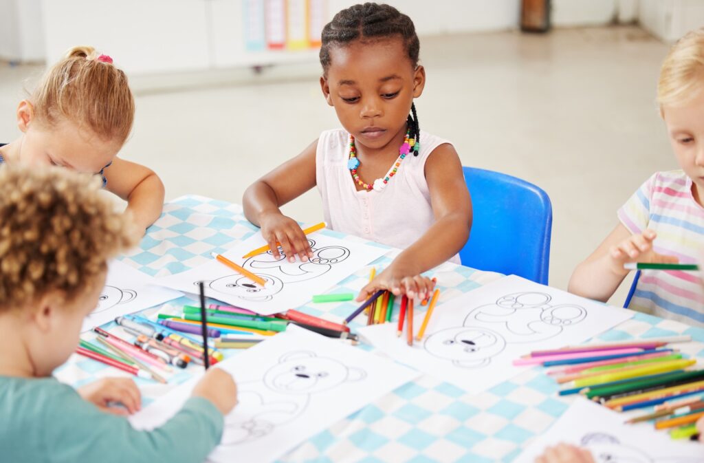 Diverse group of children sitting at a table and colouring at pre-school or kindergarten. Group of